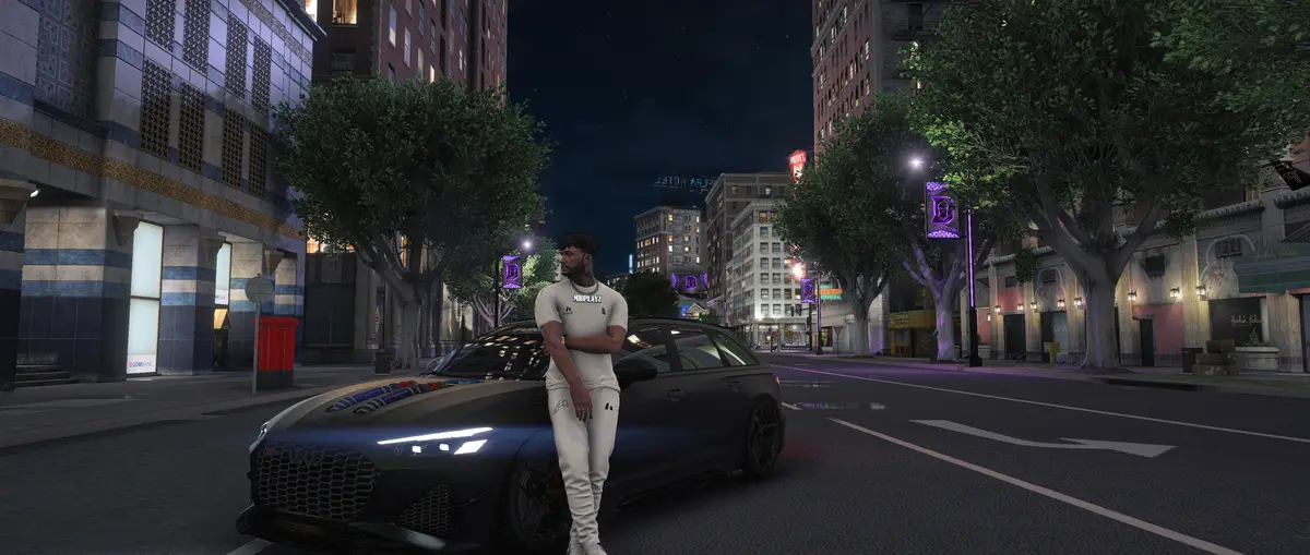 A DRILL UK player dressed in white leaning on a black car on a tree lined city street at night