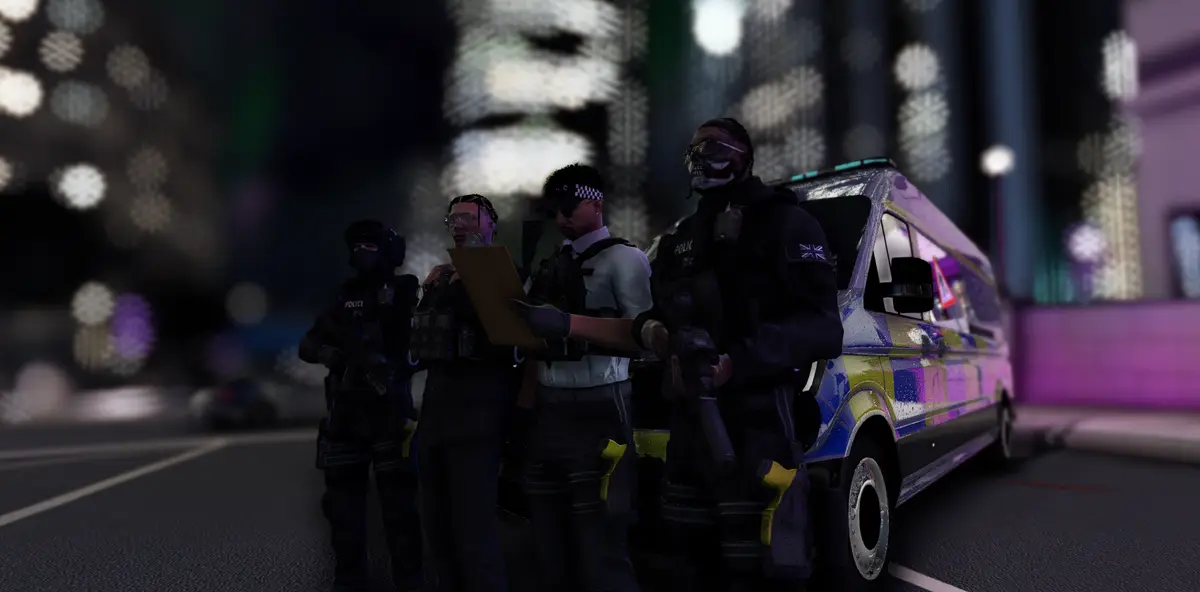 Four armed DRILL UK police officers beside their liveried van on a city street at night, one reading a clipboard